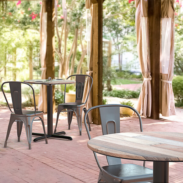 A Lancaster Table & Seating Excalibur round dining table with a textured mixed plank finish and chairs on a brick patio.