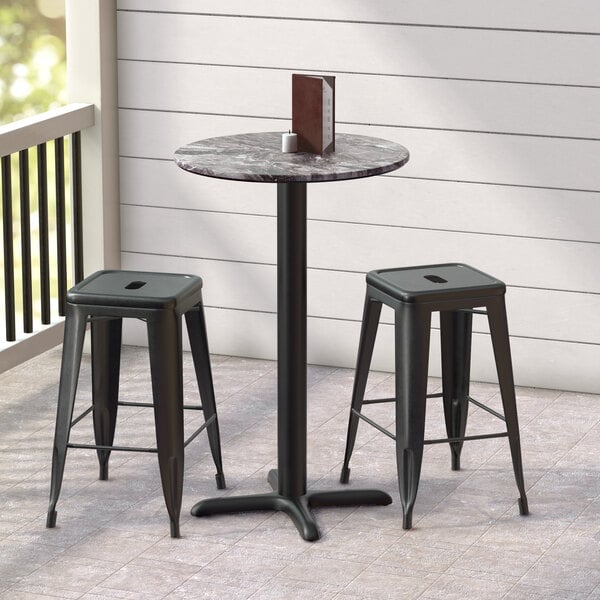 A black Lancaster Table & Seating bar table with a round top and cross base plate, with two black stools.