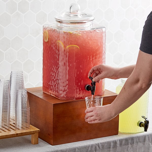 A person pouring water from an Acopa glass beverage dispenser.