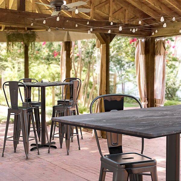 A Lancaster Table & Seating rectangular bar height table with a smooth finish and cross base plate on a covered outdoor patio with chairs.