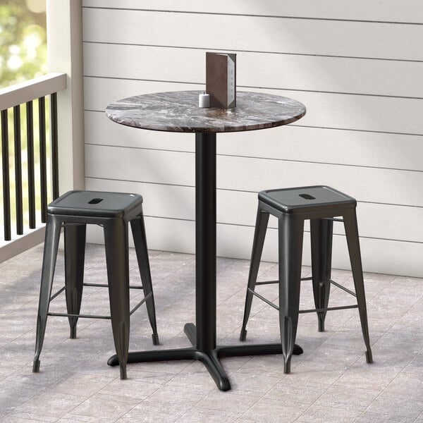 A Lancaster Table & Seating round counter height table with a cross base plate and two stools on a patio.