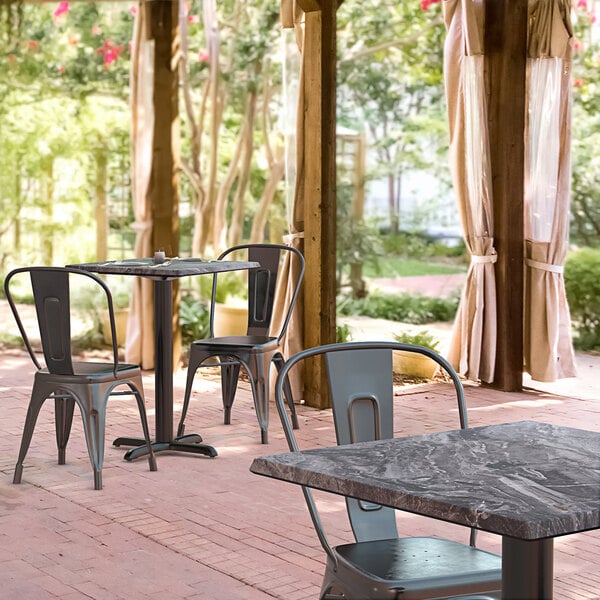 A Lancaster Table & Seating square table with a smooth finish and cross base plate on an outdoor patio with chairs.