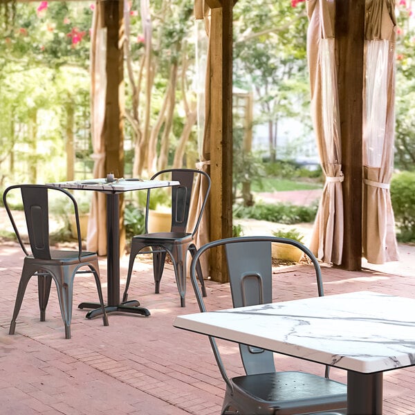 A Lancaster Table & Seating square dining table with a smooth finish and cross base plate on a brick patio with chairs.