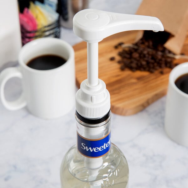 A white Tablecraft coffee syrup pump on a bottle of coffee syrup next to a coffee maker.