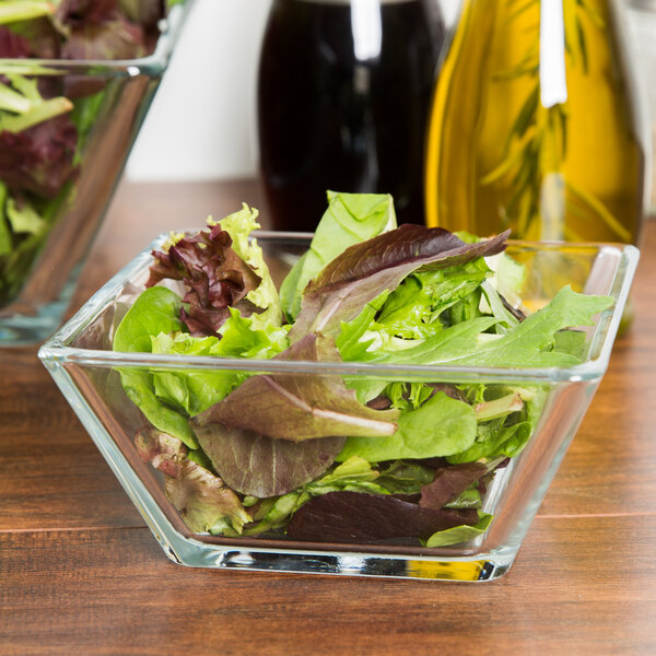 A bowl of salad in a Libbey square glass bowl on a table.