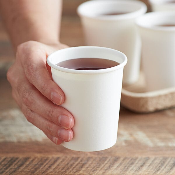 A hand holding a white Choice paper cold cup filled with liquid.