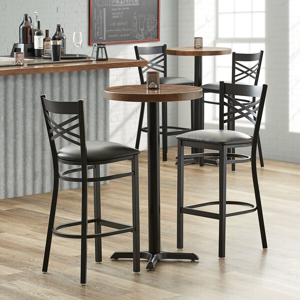 A Lancaster Table & Seating round wood butcher block table top with vintage finish on a table with three black bar stools.