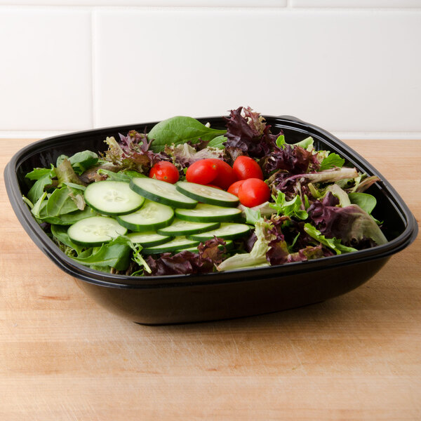 A salad with cucumbers and tomatoes in a black Sabert Catering Bowl on a counter.