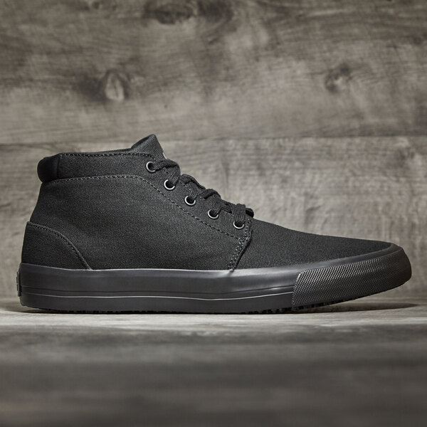 A black canvas Shoes For Crews Cabbie II men's shoe with a black rubber sole on a wood surface.