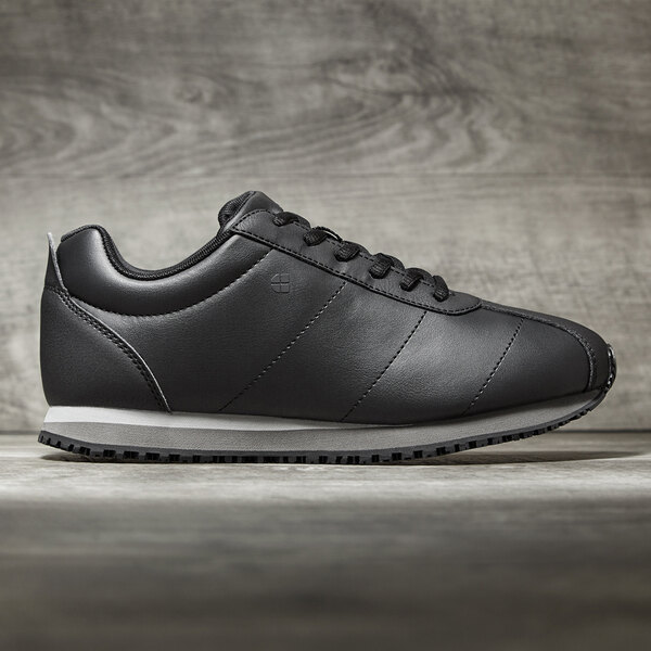 A black Shoes For Crews women's athletic shoe with a white sole.