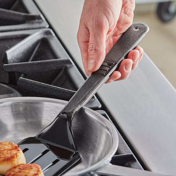 A person using a Carlisle black slotted spatula to cook scallops.