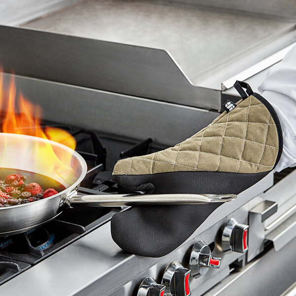 A person wearing a San Jamar Best Grip oven mitt holding a pan of food over a pot on the stove.