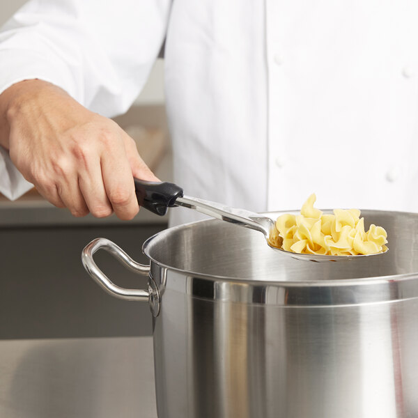 A person using a Vollrath Jacob's Pride slotted basting spoon to stir pasta in a large pot.