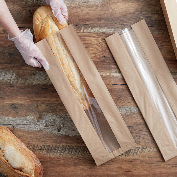 A person holding a Durable Packaging kraft paper bag with a window containing a loaf of bread.