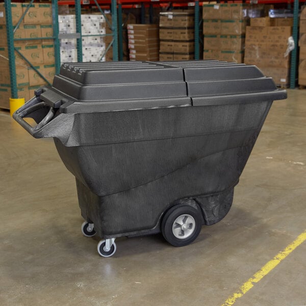 A large black Rubbermaid tilt truck with a hinged dome lid sits in a warehouse.