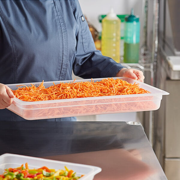 A woman holding a Cambro translucent polypropylene food pan full of shredded carrots.