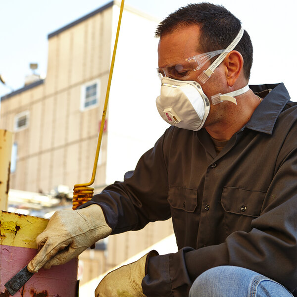 A man wearing a 3M P100 particulate respirator and gloves is working on a piece of equipment.