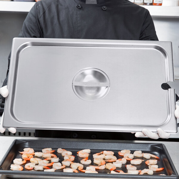 A chef holding a Vollrath stainless steel pan of shrimp over a stove.