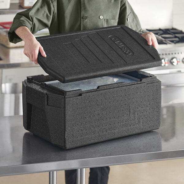 A hand opening a black Cambro food pan carrier with a translucent food pan and seal cover inside.