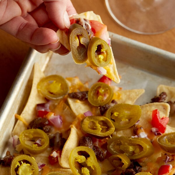 A person holding nachos with jalapenos and cheese.