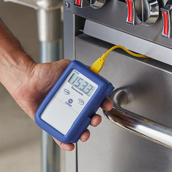A person in a professional kitchen holding a Comark Type-K thermocouple thermometer.