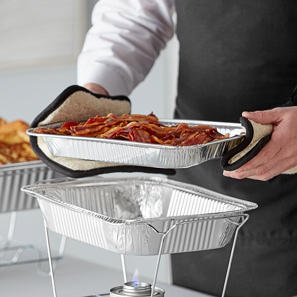 A person holding a metal tray of food over a shallow foil steam table pan.