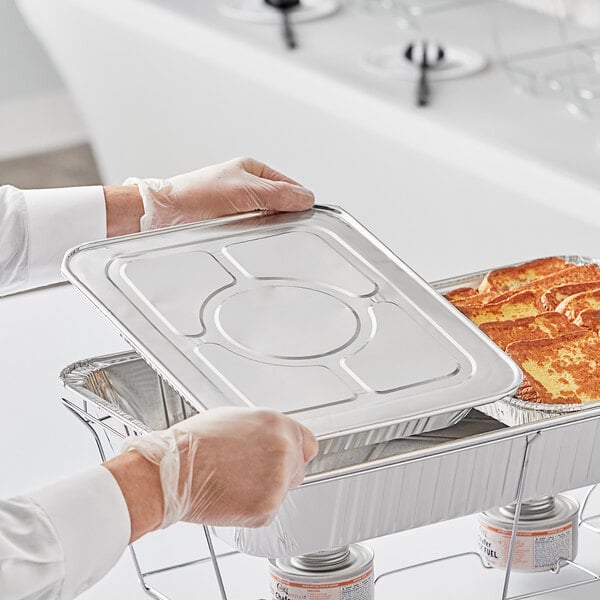 A person in gloves putting french toast into a Choice half size foil steam table pan lid.