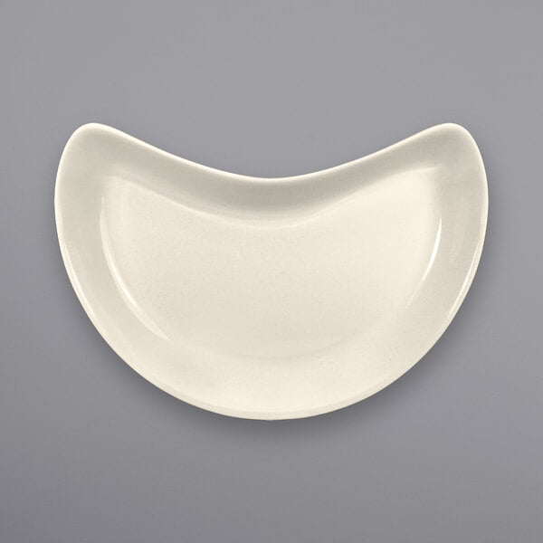 A white International Tableware stoneware crescent dish with a curved edge.
