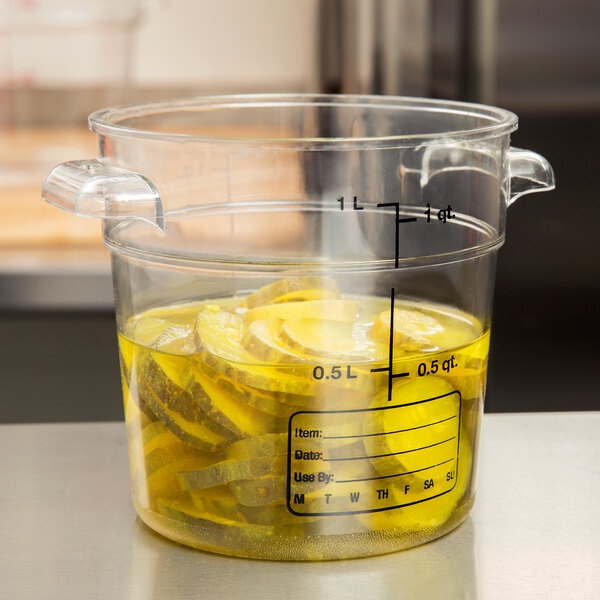 A close up of a Carlisle clear round polycarbonate food storage container filled with pickles.