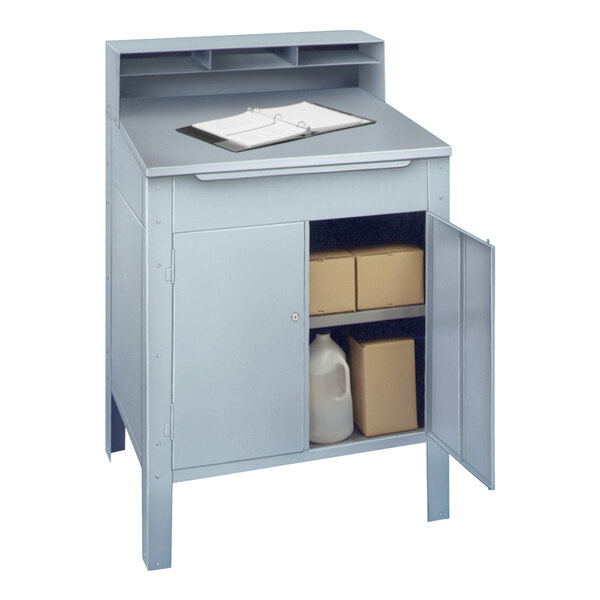 A Winholt stainless steel receiving desk with a clipboard on a shelf above a grey cabinet with a carton.