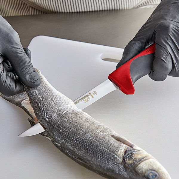 A person using a Dexter-Russell narrow flexible boning knife with a red handle to cut a fish.