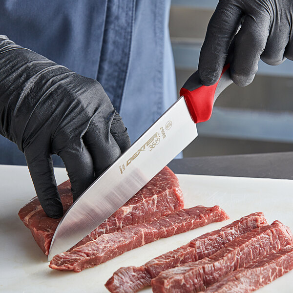 A person's hand in a black glove using a Dexter-Russell Santoku knife to cut raw meat.