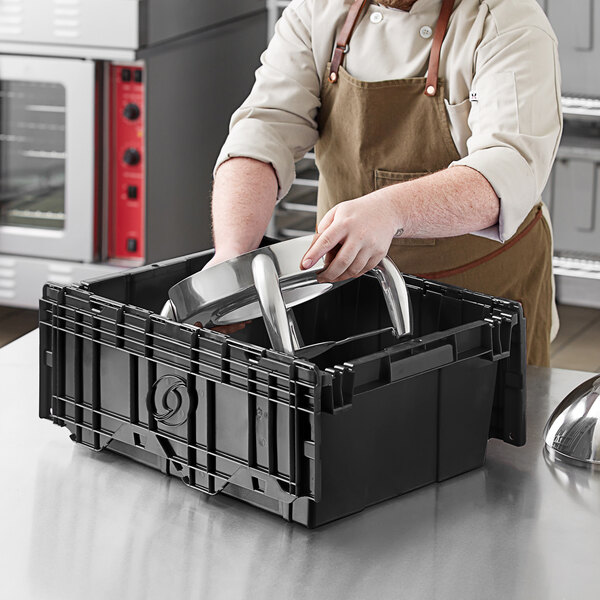 A man in an apron placing a metal object in a black Orbis tote box with a hinged lid.