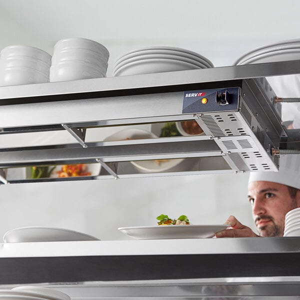 A man in a white chef's hat using a ServIt double strip warmer to heat a plate of food.