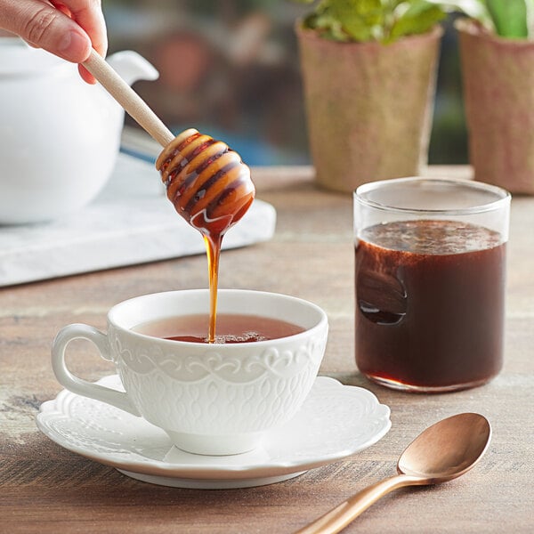 A person pouring Monarch's Choice buckwheat honey into a cup of tea.