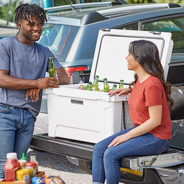 A man and woman sitting on the back of a truck with a white CaterGator cooler.