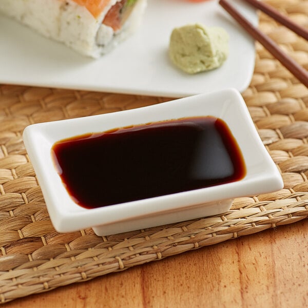 A white rectangular container of Lee Kum Kee Premium Soy Sauce with brown liquid inside on a place mat.