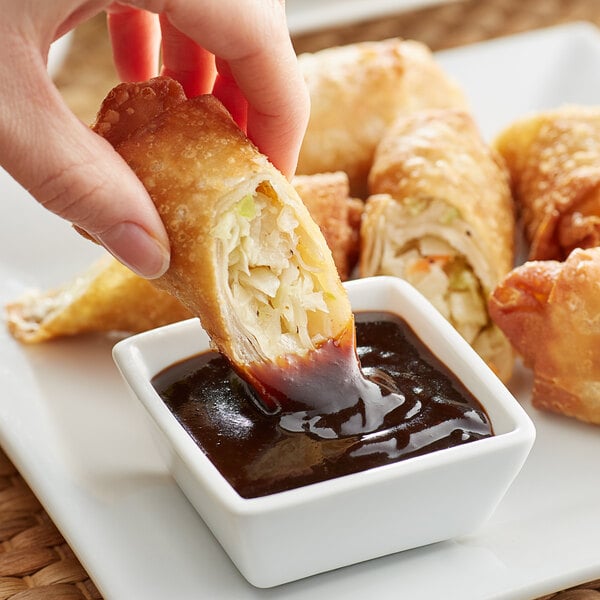 A hand dipping a fried spring roll into Lee Kum Kee hoisin sauce.