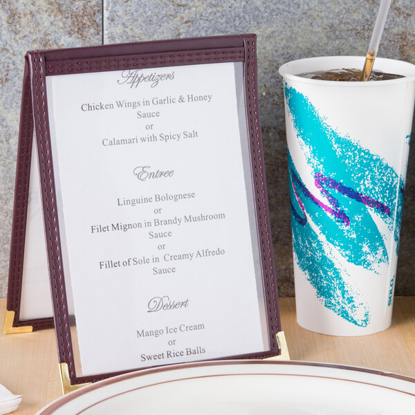 A Menu Solutions burgundy sewn edge table tent on a table with a cup and a plate.