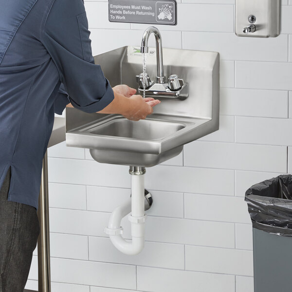 A person washing their hands in a Regency wall mounted hand sink under a running water faucet.