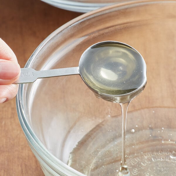 A hand using a spoon to pour liquid from a Golden Barrel 5 gallon medium invert sugar pail into a bowl.