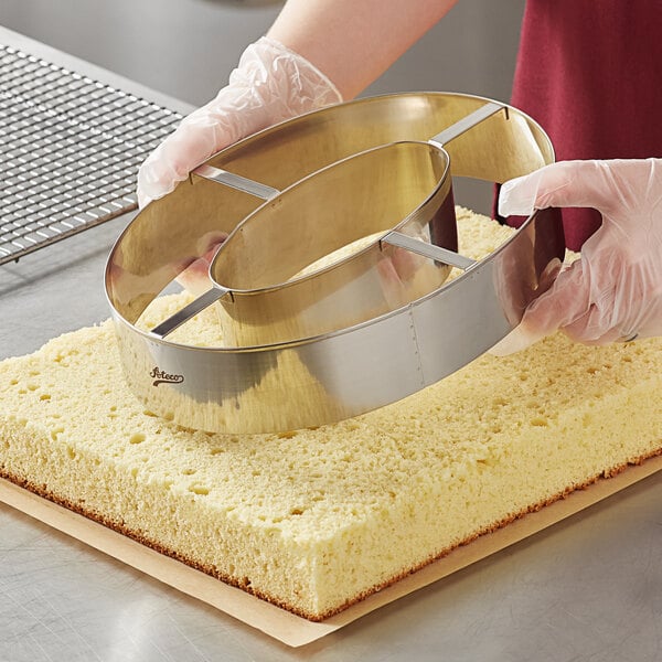 A person using an Ateco stainless steel number 0 cutter to cut a cake.