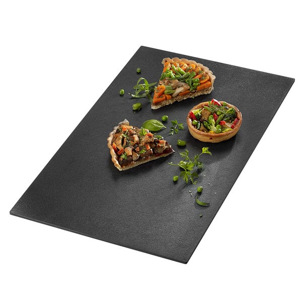 A Solia slate black tray with a slice of pizza with vegetables on it.