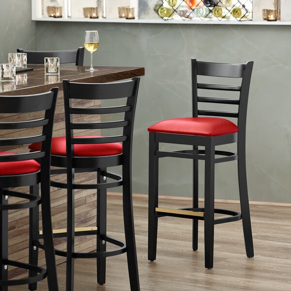 A Lancaster Table & Seating black wood bar stool with red vinyl seat and ladder back.