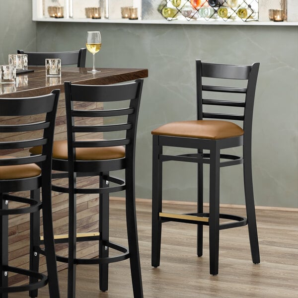 A Lancaster Table & Seating wood ladder back bar stool with a light brown vinyl seat.