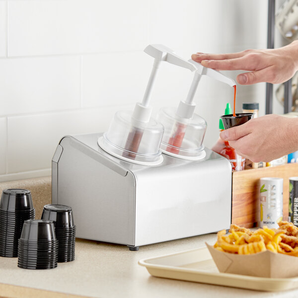 A person using a Steril-Sil stainless steel condiment dispenser to pour sauce into white containers.