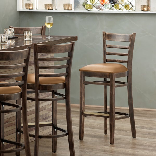 A Lancaster Table & Seating wood bar stool with a light brown vinyl cushion on the seat at a restaurant table.