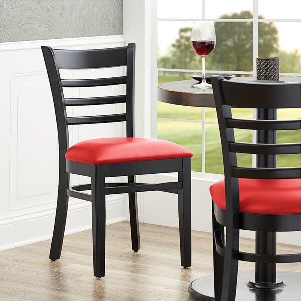 A Lancaster Table & Seating black wood ladder back chair with a red vinyl seat.