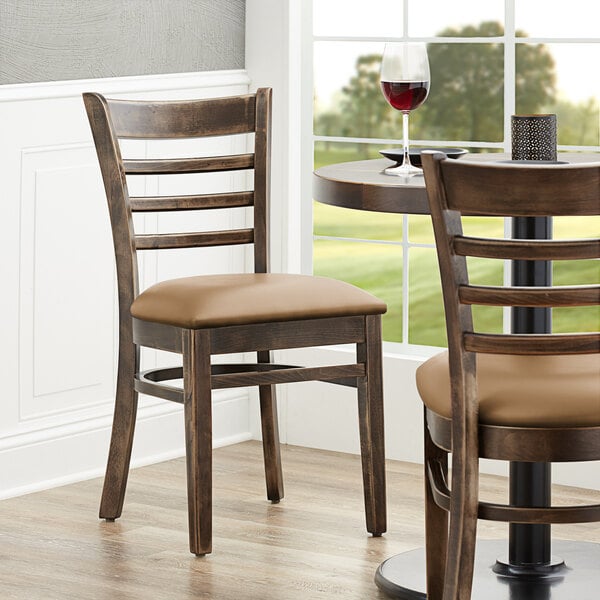 A Lancaster Table & Seating wood ladder back chair with a light brown vinyl seat on a table in a restaurant dining area.