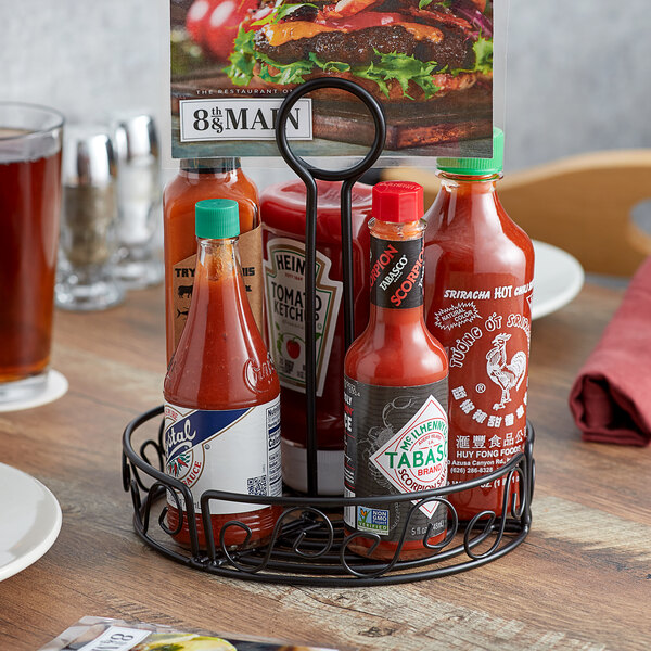 A group of hot sauces in a black metal holder on a table.